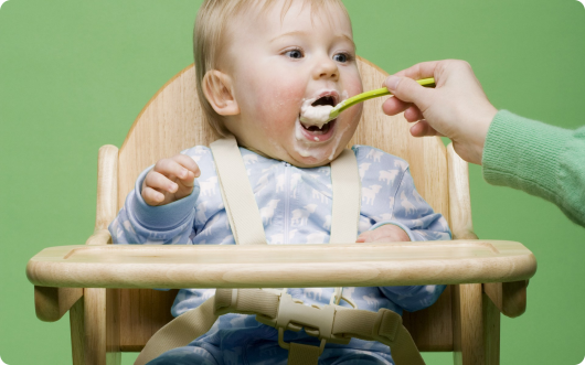 ребенка в стульчике кормят с ложечки